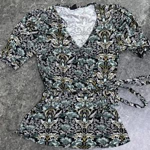 Blommig omlottopp från Gina Tricot XS - Supersnygg omlottopp från Gina Tricot i svart med blommigt mönster i grönt, vitt och gult. Toppen har v-ringning, knytband i midjan och korta ärmar. Perfekt för dig som gillar detaljer och mönster!