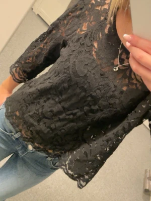 Svart spetsblus Flash Woman - En svart blus från Flash Woman i storlek M. Blusen är helt i spets med blommigt mönster och har trekvartsärm. Den är lite genomskinlig och har en rund halsringning. Använd runt 1 eller 2 gånger.