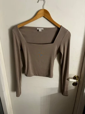 Beige långärmad topp från Amisu - Säljer en beige långärmad topp från Amisu med fyrkantig urringning och croppad passform. Toppen är enkel och stilren, tillverkad i mjukt stretchigt material som sitter snyggt på kroppen. Perfekt att matcha med höga jeans eller kjol.