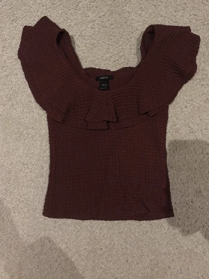 Vinröd volangtopp från Lindex - Supersöt vinröd topp från Lindex med volangdetalj runt axlarna och en smockad, stretchig struktur. Toppen är ärmlös och har en croppad passform som sitter snyggt på kroppen. 