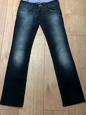 Svarta Lee jeans Low Rise - Säljer ett par svarta Lee jeans med snyggt slitna detaljer och raka ben. (W26 L33)Klassisk femficksmodell med Lee-lapp bak i midjan och kontrastsömmar på bakfickorna. Jeansen har normal passform och är tillverkade i slitstarkt denimtyg. LOW RISE