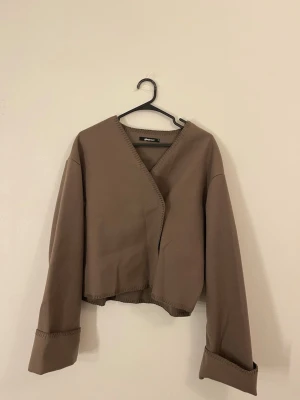 Brun jacka från Gina Tricot - Säljer en brun jacka/kofta från Gina Tricot med omlott-design och knappar framtill. Den är aldrig använd - har inga noppror i tyget!!