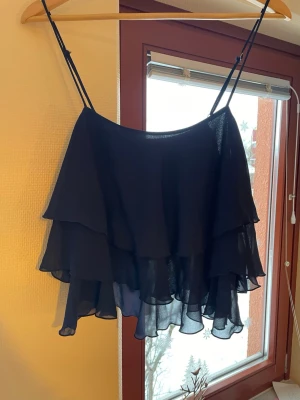 Marinblå volang topp - Säljer en marinblå topp med tunna axelband och flera lager volanger. Toppen är luftig och har en flowy känsla, perfekt för varma dagar.