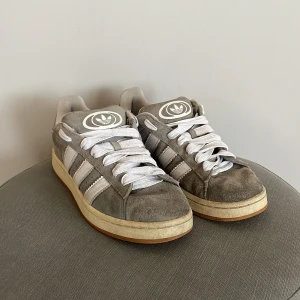 Grå Adidas Campus 00s - Säljer ett par grå Adidas Campus 00s i storlek 43 & 1/3. Stora i storleken så passar även storlek 44. Märkbart använda och slitage från användning förekommer, men inga brister i funktionen. Saknar original-låda till skorna.