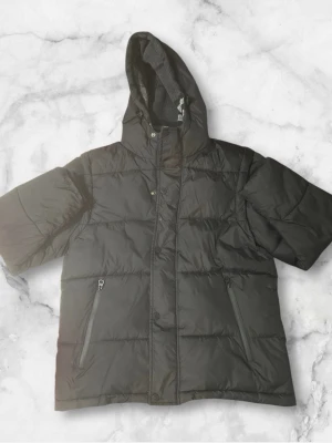 Svart pufferjacka från Burberry - Säljer en svart pufferjacka från Burberry London England. Jackan har huva, dragkedja och knappar framtill samt två fickor med dragkedja. Insidan har ett rutigt foder i grå toner. Perfekt för kalla dagar och riktigt snygg streetstil.