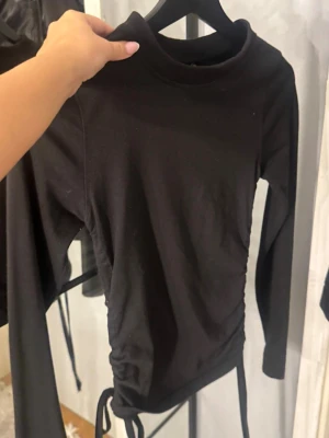 Svart långärmad topp med snörning - Snygg svart långärmad topp med hög hals och snörning i sidorna som ger en cool rynkad effekt. 