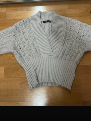 Ljusgrå ribbad kofta från SHEIN - Ljusgrå kofta från SHEIN i storlek S med bred ribbad mudd i midjan och vid kragen. Koftan har ett stickat mönster över hela plagget och djup v-ringning. Perfekt för lager på lager under höst och vinter.