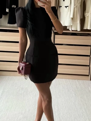 Svart kort klänning med puffärm från Zara  - Säljer en svart kort klänning med markerad midja och puffiga axlar. Klänningen har en stilren, figurnära passform och korta ärmar. Perfekt för dig som gillar minimalistisk och chic stil. Använd en gång! Storlek xs