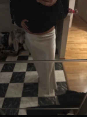Lång vit satinkjol - Säljer en lång, vit kjol i satinliknande material. Kjolen har en enkel och stilren design med resår i midjan och ett mjukt, glansigt tyg som faller snyggt längs benen. Perfekt för dig som gillar minimalistisk och elegant stil. Pris kan diskuteras 