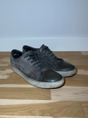 Grå Lanvin med mocka och lackdetalj - Säljer ett par grå lanvin med ovandel i mocka och snygga lackade tår. Skorna har snörning och vit platt sula. Perfekta för vardagligt bruk men även till finare tillfällen. Storleken är egentligen 43 men sitter som 44or. Tveka inte om att höra av dig vid eventuella frågor! Priset är inte hugget i sten.