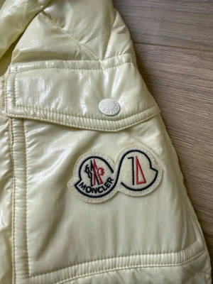  Moncler pufferjacka - Säljer en creamfärgad pufferjacka från Moncler med quiltad design och hög krage. Jackan har tryckknappar, fickor och Moncler-logga på ärmen. Materialet är glansigt och känns riktigt lyxigt, perfekt för kalla dagar. Pris kan diskuteras 