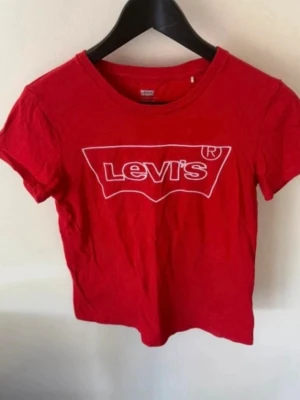 Röd Levi's t-shirt med logga - Snygg röd t-shirt från Levi's med klassisk vit logga framtill. T-shirten har rund hals och korta ärmar, perfekt för en avslappnad och cool stil. Tillverkad i mjuk bomull som känns skön mot huden.
