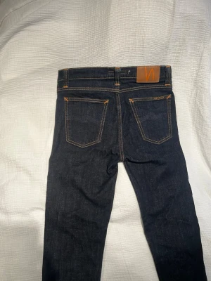 Nudie Jeans herr W29/L32 - Säljer ett par mörkblå Nudie Jeans Tube Tom med klassisk orange söm och läderpatch bak. Jeansen har fem fickor, raka ben och är tillverkade i kraftigt jeansmaterial. Perfekta för dig som gillar stilrena och tidlösa jeans. Använda endast några gångar, och parfekt för dig som vill göra egna slitningar eller tvätta den mer💪