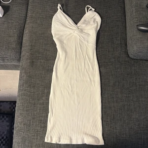 Vit ribbad klänning från Bik Bok - Säljer en vit ribbad klänning från Bik Bok i storlek XS. Klänningen har smala axelband, twistad detalj framtill och är figurnära med en kort längd. Perfekt för sommarens alla tillfällen!