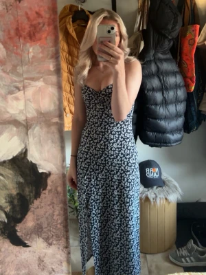 Svart långklänning med blommigt mönster - Supersnygg svart långklänning med vita små blommor och v-ringning. Klänningen är ärmlös med smala axelband och har en lätt slits framtill. Perfekt för varma dagar och har en feminin, figurnära passform. Har även slits längst ner på klänningen, som man kan se på en av bilderna. Använd endast en gång på midsommar!💞💞