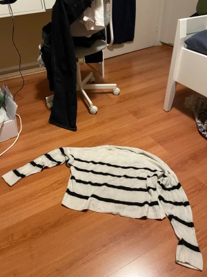 Randig beige tröja med svarta ränder - Säljer en beige stickad tröja med svarta horisontella ränder. Tröjan har lång ärm och ribbade muddar vid ärmslut och nederkant. Perfekt för dig som gillar en enkel men snygg look. Från 