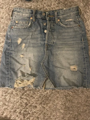 Blå jeanskjol  från A Denim - Säljer en blå jeanskjol från A Denim.Kjolen har knappgylf, fem fickor och klassisk denimlook. Perfekt för dig som gillar en avslappnad och trendig stil.