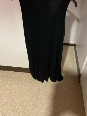 Svart långklänning från Lindex - En svart långklänning från Lindex i storlek L. Klänningen är ärmlös och har en enkel, rak siluett som ger en clean och stilren look. Perfekt för dig som gillar minimalistisk stil och vill ha något som funkar till många tillfällen. Viscos. Säljs på fler sidor. 
