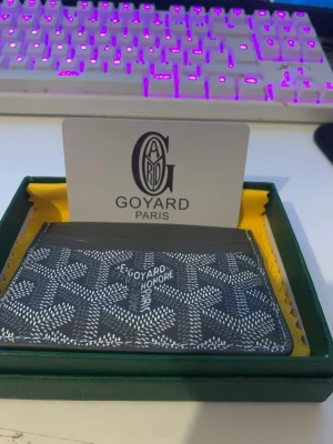 Grå mönstrad plånbok från Goy4ard - Säljer en stilren grå plånbok från Goy4ard med det klassiska vita grafiska mönstret och logga framtill. Plånboken har flera fack för kort och är tillverkad i ett tåligt material. Kommer i original ask med gul tygpåse.