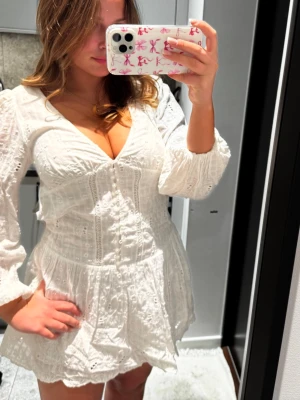 Student klänning  - Superfin vit kort klänning från Zara med broderade spetsdetaljer, v-ringning och långa puffärmar. Klänningen har knappar framtill och en lätt volang i kjolen. Perfekt för sommarens alla tillfällen!