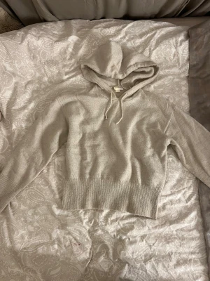 Beige stickad hoodie med huva - Mysig beige stickad hoodie med huva och dragsko. Tröjan har bred ribbstickad kant nedtill och vid ärmsluten, samt långa ärmar. Perfekt för lager på lager och chill dagar. Materialet ser ut att vara mjukt och skönt.