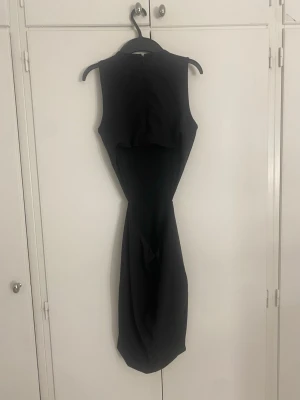 Svart ärmlös klänning med öppen rygg - Säljer en svart, ärmlös klänning med en unik öppen rygg och figurnära passform. Klänningen har rund halsringning och ett draperat fall nedtill. Perfekt för dig som gillar stilrena och moderna plagg.Använd en gång 