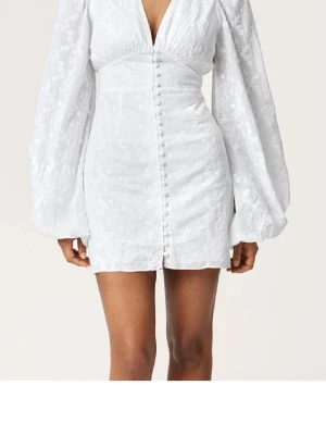 Vit kort klänning från Adoore med puffärm - Supersnygg vit kort klänning med puffiga långärmar och v-ringning från Adoore. Klänningen har knappar framtill och ett subtilt blommigt mönster i tyget. Passar mig som bär xs/s