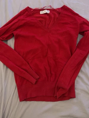 Röd stickad tröja från Zara - Röd stickad tröja från Zara med v-ringning och långa ärmar. Tröjan är tillverkad i en mjuk bomulls- och nylonblandning och har ribbade muddar vid ärmslut och nederkant. Perfekt för lager-på-lager och enkel att matcha.