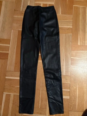 Svarta leggings/byxor i skinnimitation - Snygga svarta leggings/byxor i skinnimitation med hög midja och tight passform. Lite fodrade. Nya med prislapp kvar
