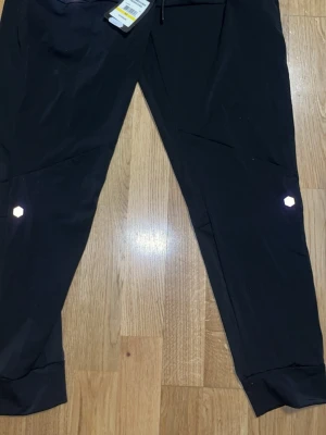 Svarta träningsbyxor från Under Armour - Svarta träningsbyxor från Under Armour med reflekterande detaljer på benen. Byxorna är tillverkade i ett lätt och ventilerande HeatGear-material som passar perfekt för intensiva träningspass. De har en lös passform och elastisk midja med dragsko.