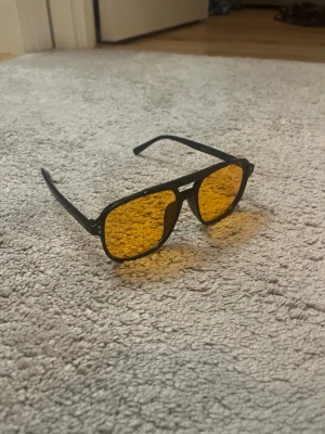 Svarta solglasögon med gula glas - Helt nya och oanvända solglasögon med svart båge och rektangulära gul/orange glas. Skriv privat för mer information 