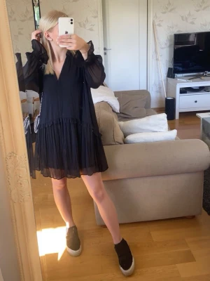 Svart volangklänning med v-ringning - Svart kortklänning med v-ringning och volangdetaljer.