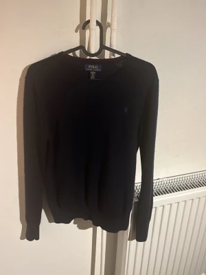 Mörkblå stickad tröja Polo Ralph Lauren - Klassisk mörkblå stickad tröja från Polo Ralph Lauren i storlek XL barn. Tröjan har rund halsringning, diskret logga på bröstet och långa ärmar. Perfekt till lager på lager under höst och vinter. Enkel och stilren design som funkar till det mesta.