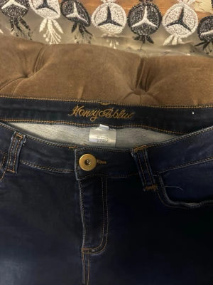Mörkblå skinny jeans från honey Blue - Snygga mörkblå skinny jeans från honey Blue med klassiska bakfickor och gylf med knapp. Jeansen har kontrastsömmar och är tillverkade i stretchigt jeansmaterial för en bekväm passform.