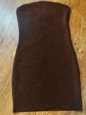 Brun glittrig klänning - Snygg brun klänning med glittrigt tyg som fångar ljuset. Perfekt för dig som vill sticka ut med en elegant och trendig look. Materialet känns mjukt och följsamt mot kroppen.