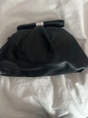 Svart Dumpling bag! - HELT NY, ALDRIG ANVÄND! Säljer den väskan på grund av att jag råkade beställa två! Stilren svart  hand väska  med mjuk, slät yta och rundad form. Väskan har ett avtagbart axelband och stängs med magnet. Perfekt för att bära det viktigaste och ger en trendig touch till din outfit. 