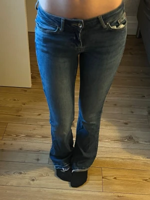 Blå bootcut jeans med låg midja - Snygga blå jeans med bootcut passform och låg midja. Jeansen har klassisk femficksdesign och är tillverkade i ett mjukt jeansmaterial. Perfekta för dig som gillar en avslappnad men ändå trendig look.