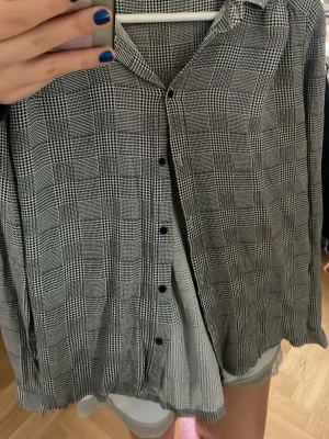 Rutig skjorta i svart och grått - Stilren rutig skjorta från minimum i svart och grått. Skjortan har klassisk krage, knappar framtill och långa ärmar med manschett. Tunt och mjukt material som ger en avslappnad känsla. Perfekt för dig som gillar tidlös stil.