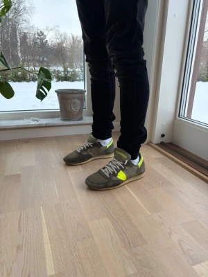 Gröna sneakers med gula detaljer - Snygga sneakers i grönt med neon-gula detaljer och vita snören. Skorna har en klassisk låg profil och platt sula, vilket ger en avslappnad look. Materialet ser ut att vara mocka och textil, perfekt för dig som gillar streetwear.