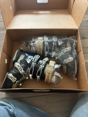 HEAD svarta pjäxor med spännen - Snygga svarta pjäxor från HEAD med beige detaljer och fyra metallspännen för perfekt passform. Insidan är vadderad för extra komfort och märket syns tydligt på remmen. Perfekta för dig som vill ha stilrena och funktionella pjäxor till skidåkningen.  Storlek 24,5. Orginalpris 3200kr