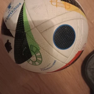 UEFA EURO 2024 fotboll - Säljer en officiell UEFA EURO 2024 fotboll med tryck från Tyskland. Bollen är vit med svarta, gröna och gula detaljer samt mönster. Perfekt för dig som älskar fotboll och vill ha en boll med snygg design och turneringskänsla.