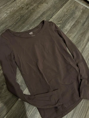 Brun långärmad topp från 157 - En enkel brun långärmad topp från 157 med rund halsringning. Tillverkad i mjukt bomullsliknande material som känns skönt mot huden. Modellen är figurnära och passar perfekt till lager på lager eller som basplagg.