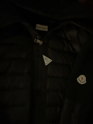 Moncler Cardigan - Snygg svart dunjacka från Moncler med klassisk quiltad design och dragkedja framtill. Jackan har Moncler-logga på ärmen och en stilren look som passar perfekt till kalla dagar.