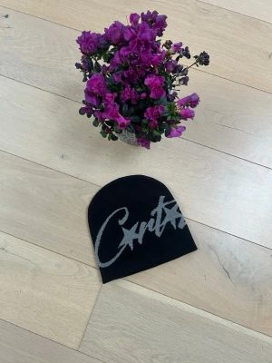 Svart mössa med grå text och stjärnor - Snygg svart mössa med grått tryck i form av text och två stjärnor på framsidan. Mössan har en klassisk, tight passform och är tillverkad i mjukt, stretchigt material som passar perfekt till höst och vinter.