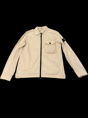 Stone Island overshirt M beige - Stone Island overshirt storlek M ljus beige äkta såklart. Har en liten fläck på ryggen (zooma bild 2) inget man tänker på i första taget. Annars är den 10/10 skick och dragkedjan funkar perfekt