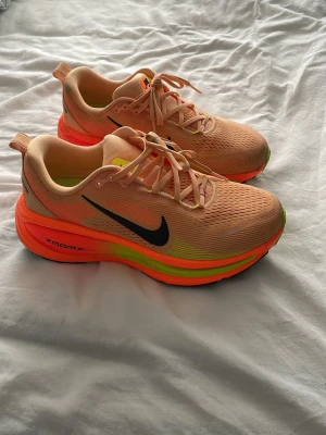 Nike Vomero 18 M löparskor i orange och neon - Nike Vomero 18 M löparskor i en fräsch ljusorange färg med neonorange och limegröna detaljer. Skorna har svart swoosh-logga på sidan, snörning och ventilerande meshmaterial. Mellansulan är extra tjock för maxad dämpning och energiåtergivning, perfekt för träning och löpning. Storlek Medium och använd max 5 gånger så den är i bra skick med lite små fläckar på. Sko kartongen finns inte kvar.