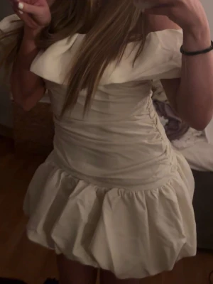 Krämvit kort volangklänning - NYPRIS 550. Supersöt krämvit kort klänning med volangdetaljer och bred offshoulder-krage. Helt ny med prislapp för ja råka beställa två st. Uk storlek 10 vilket e typ 36-38 