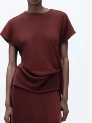 Brun topp med knyt från Zara - Snygg brun topp från Zara med korta ärmar och trendig knytning i midjan. Toppen har en enkel, stilren design och är gjord i mjukt bomullsmaterial. Perfekt att styla med både jeans och kjol för en cool look. Pris går att diskutera 