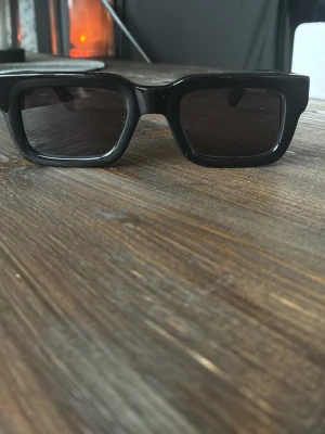 Svarta 05 glasögon från chimi  - Stilrena svarta solglasögon med rektangulära bågar i plast. Glasen är mörkt tonade och ramen är bred, vilket ger en modern och trendig look. Perfekta för att lyfta din outfit med en cool vibe. Andvända 3-4 gånger då jag impulsköpte dom o inte tänkte riktigt innan. Allting följer med så som box,duk och påse.