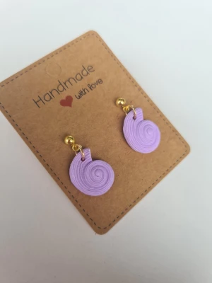 Lila handgjorda snäckörhängen - Unika snäckformade/fossilformade handgjorda örhängen i ljuslila färg med guldiga kulstift. Gjorda för hand av mig i polymerlera. 